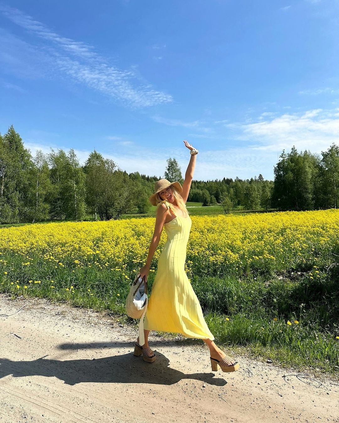 vestido longo amarelo posando em um campo florido. O look é complementado por sandálias plataforma, chapéu de palha e uma bolsa de mão, perfeito para dias ensolarados e passeios ao ar livre. desodorante com niacinamida