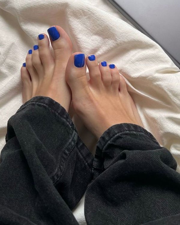 Unhas dos pés pintadas de azul vibrante, moda manicure contemporânea. Vestindo calça preta, estilo casual e descontraído, ideal para o dia a dia. Elegância simples com toques de tendência moderna em cuidados pessoais.