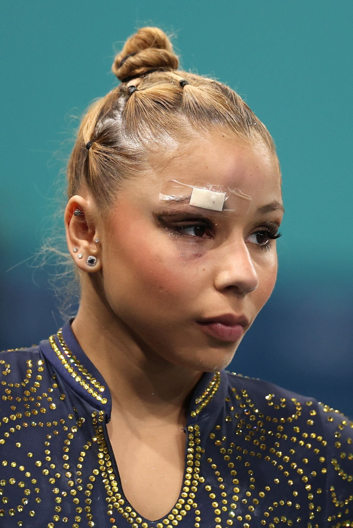 Imagem de uma mulher usando um traje esportivo azul marinho detalhado com pedrarias douradas, tendência que combina elegância e função no vestuário atlético. Ela usa cabelo preso em um coque alto. olimpíadas 2024