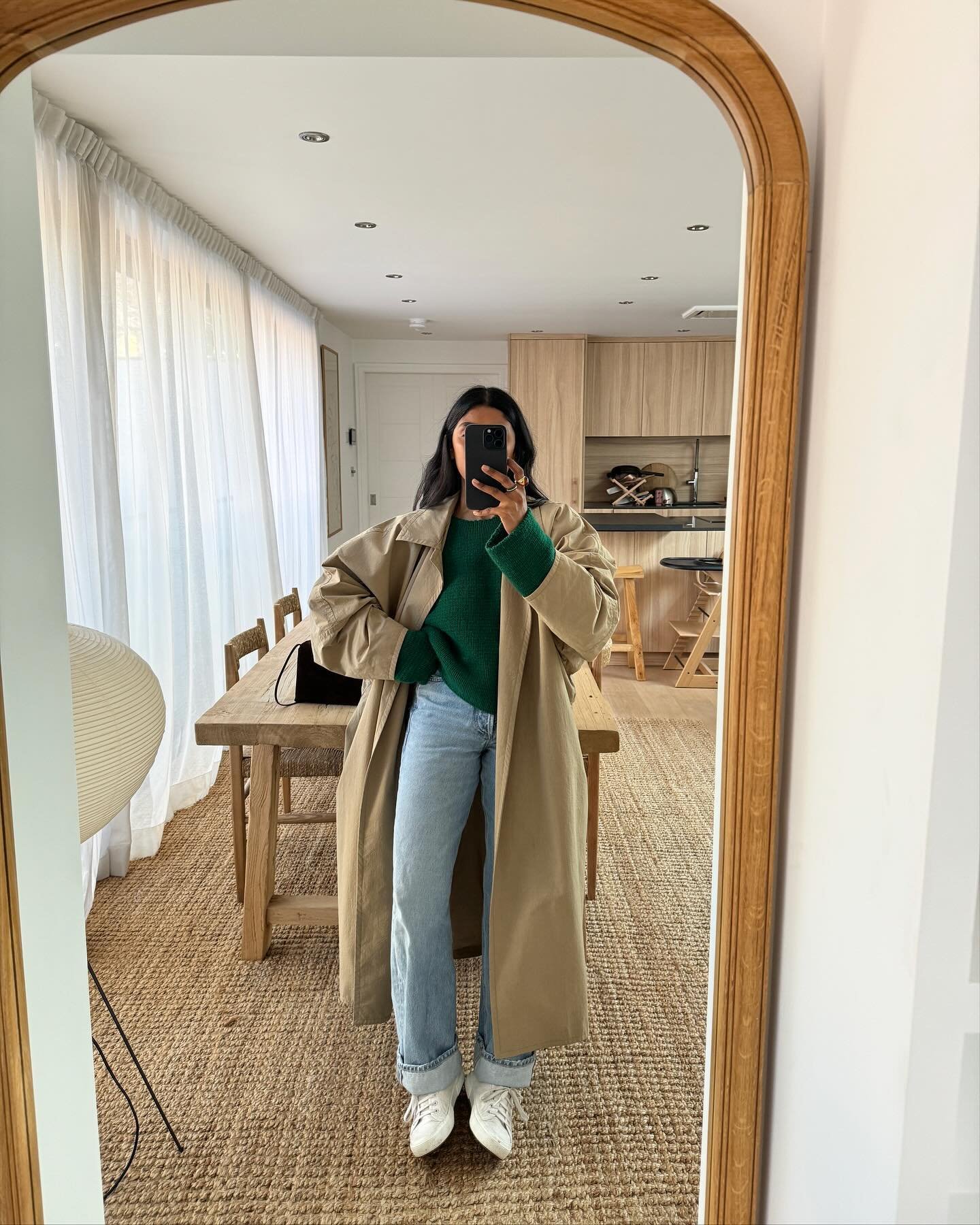 Pessoa usando trench coat bege oversized, suéter verde, jeans reto de lavagem clara e tênis branco. Look casual e moderno, perfeito para dias frescos, combinando tendências de moda como sobreposição e peças confortáveis. Estilo minimalista e elegante.