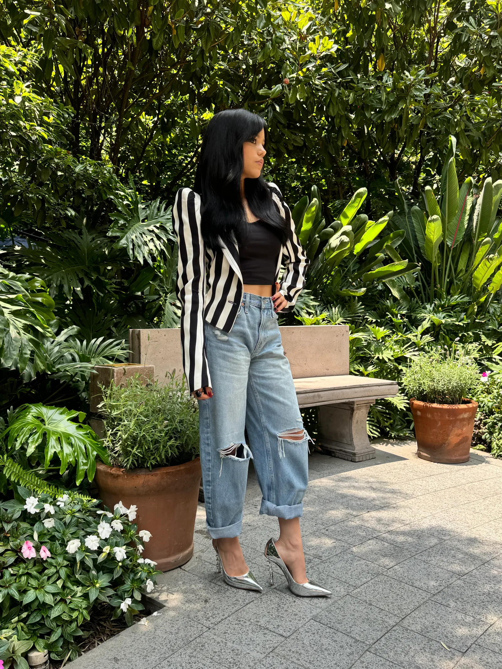 Mulher usando blazer listrado preto e branco, cropped preto e jeans rasgados estilo boyfriend. Completa o look com sapatos de salto prata.