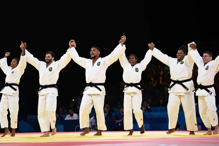 Judocas brasileiros celebrando, vestindo o tradicional judogi branco com faixas pretas, representando a equipe do Brasil. Cada uniforme possui um brasão do país no peito esquerdo, destacando a identidade nacional no esporte.