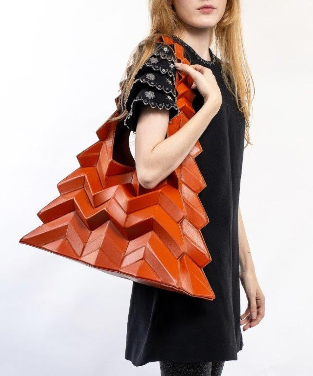 Moda: Mulher com vestido preto simples e mangas com aplicações de renda e detalhes florais. Bolsa grande laranja com design geométrico 3D em alta relevo. Tendência moderna e futurista, destacando acessórios ousados para contrastar peças básicas.