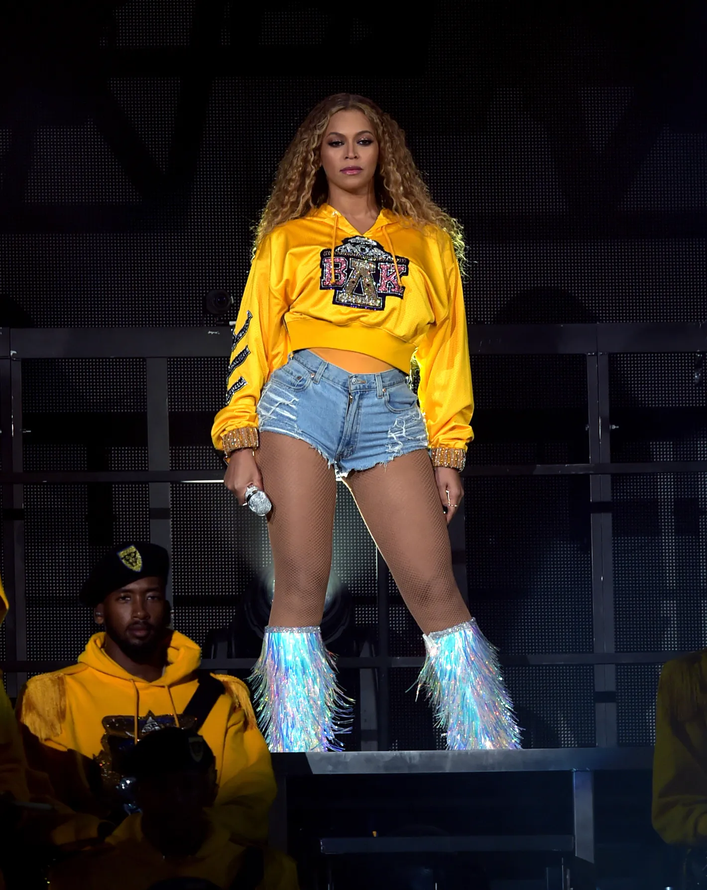 Cantora usa moletom amarelo bordado, shorts jeans rasgados e botas com franjas brilhantes. Looks da Beyoncé.