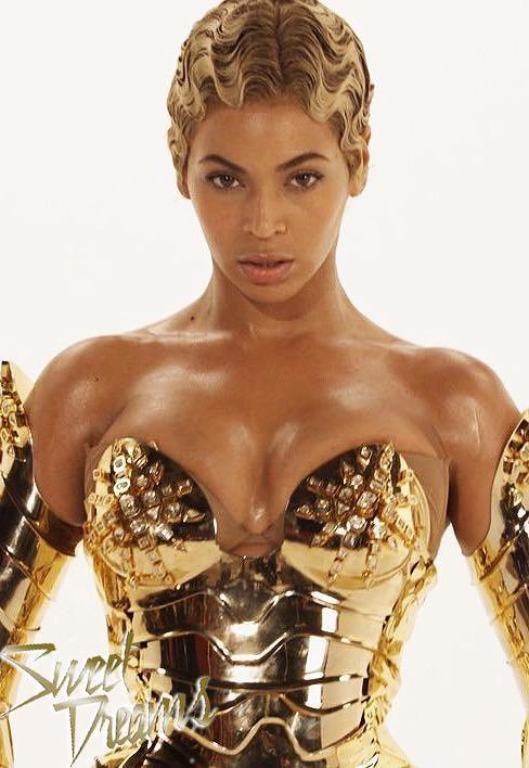 Imagem de uma mulher com cabelo ondulado e curto, vestindo um espartilho dourado com aplicações metálicas, estilo futurista e glamouroso. Looks da Beyoncé.