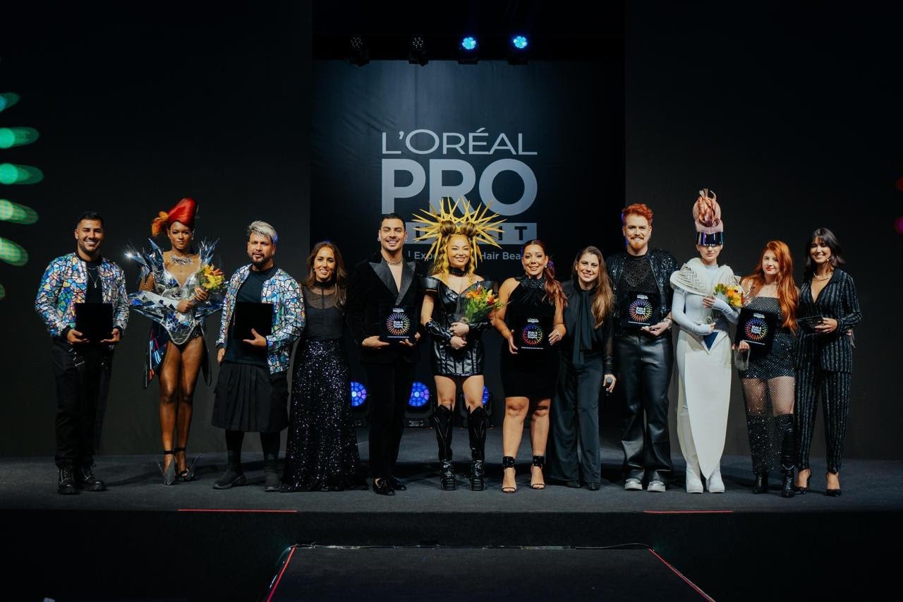 L’Oréal PRO Summit destacando tendências futuristas e elegantes. Participantes com trajes brilhantes, metalizados e estruturados. Acessórios chamativos como capacetes e adornos de cabeça.