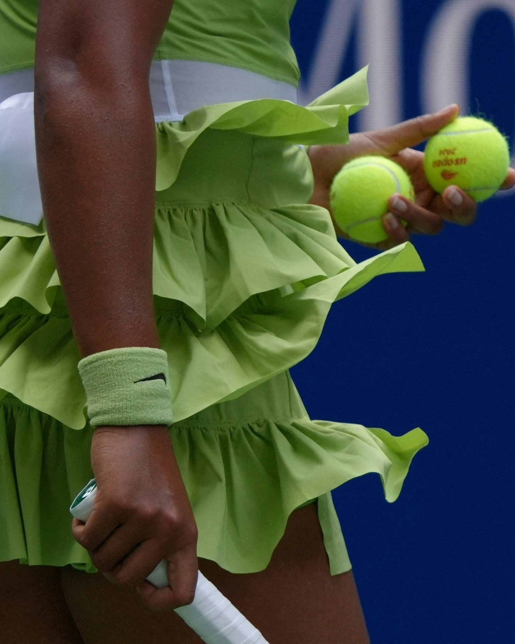  Naomi Osaka de tenista usando roupa verde com saia de babados, munhequeira combinando e segurando duas bolas de tênis. Estilo esportivo e moderno, destacando-se por suas cores vibrantes e design elegante, ideal para usos em competições e atividades físicas.