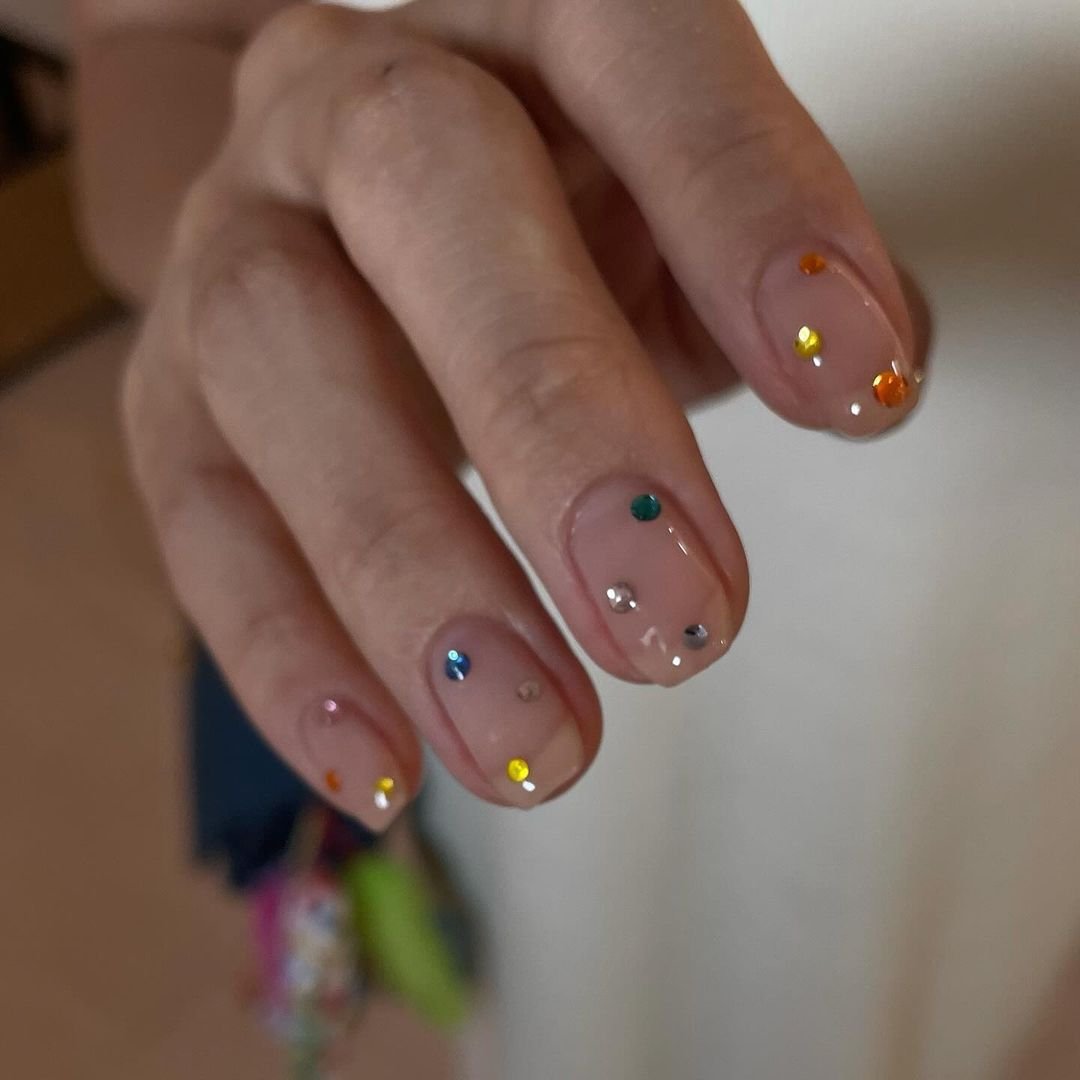 tendências de nail art com esmalte nude e pedrarias coloridas, adicionando um toque sofisticado e moderno. Tendência minimalista e elegante, perfeita para qualquer ocasião. A moda atual valoriza a simplicidade com detalhes que destacam a personalidade.