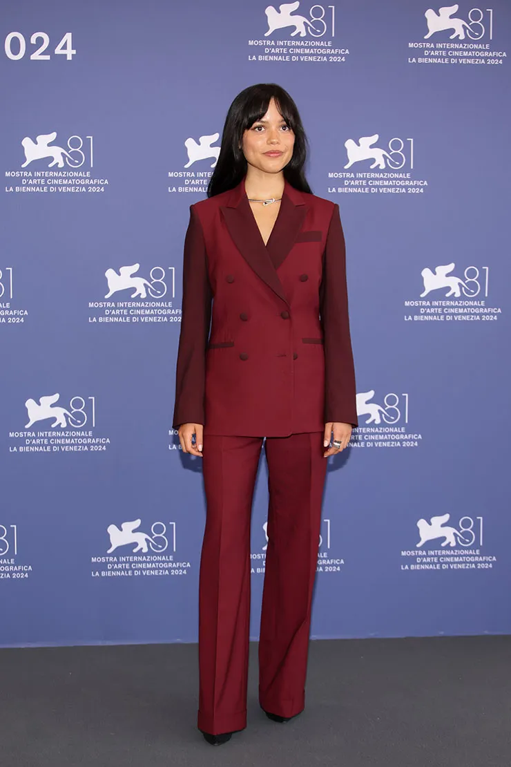 Pessoa vestida com um elegante blazer vinho de abotoamento duplo e calça de alfaiataria combinando. O look é sofisticado e moderno, adequado para eventos formais.