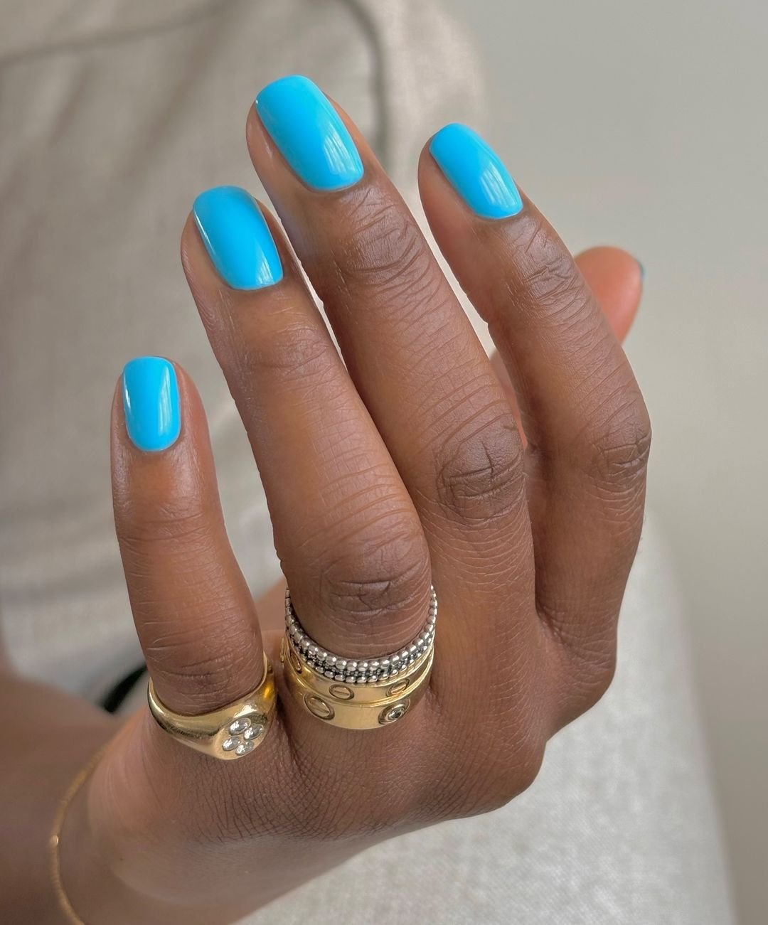 Unha pintada em tom azul vibrante, tendência moderna de nail art. Anéis dourados com detalhes em prata e pedras, estilo sofisticado e chique. A combinação destaca-se pelo contraste entre os acessórios luxuosos e a cor ousada das unhas encravadas