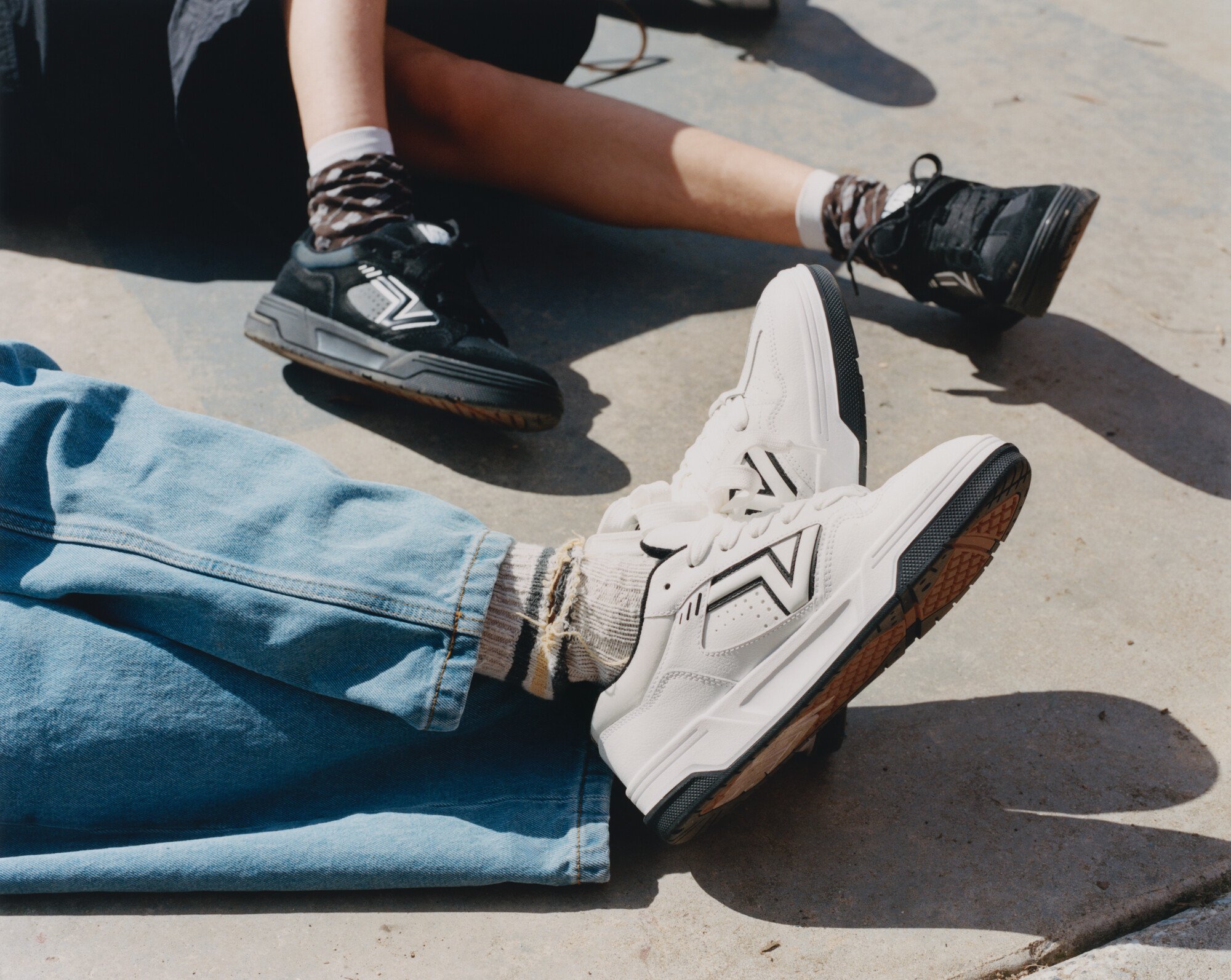 Jovens vestindo tênis esportivos modernos com design arrojado. Um par de tênis preto e outro branco, ambos com meias de estilos únicos. Calças jeans largas e shorts completam o visual casual. Tendência streetwear com foco no conforto e estilo urbano.