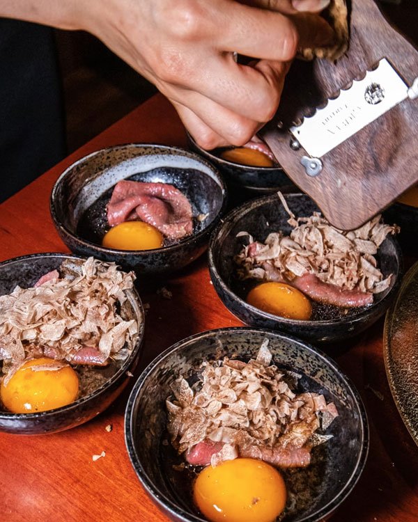 Imagem de pratos gourmet, apresentando gemas de ovo cruas, carne e lascas de trufas. Mãos de chef finalizam com lâmina de trufa. Tendência moderna em culinária de alta gastronomia.