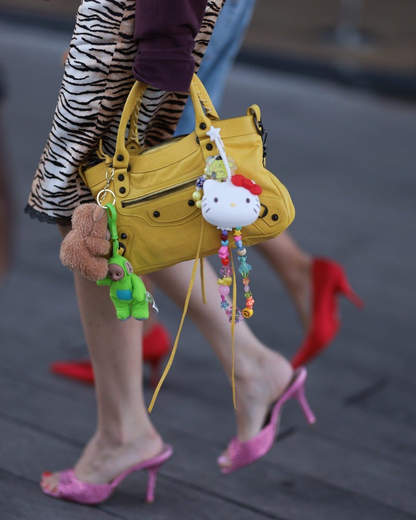 Look fashion urbano e divertido: bolsa amarela com chaveiros fofos, incluindo Hello Kitty e Teletubbies; saia com estampa de zebra; sapatos de salto alto rosa brilhoso e vermelho vibrante. Ideal para quem busca um estilo único e descontraído.