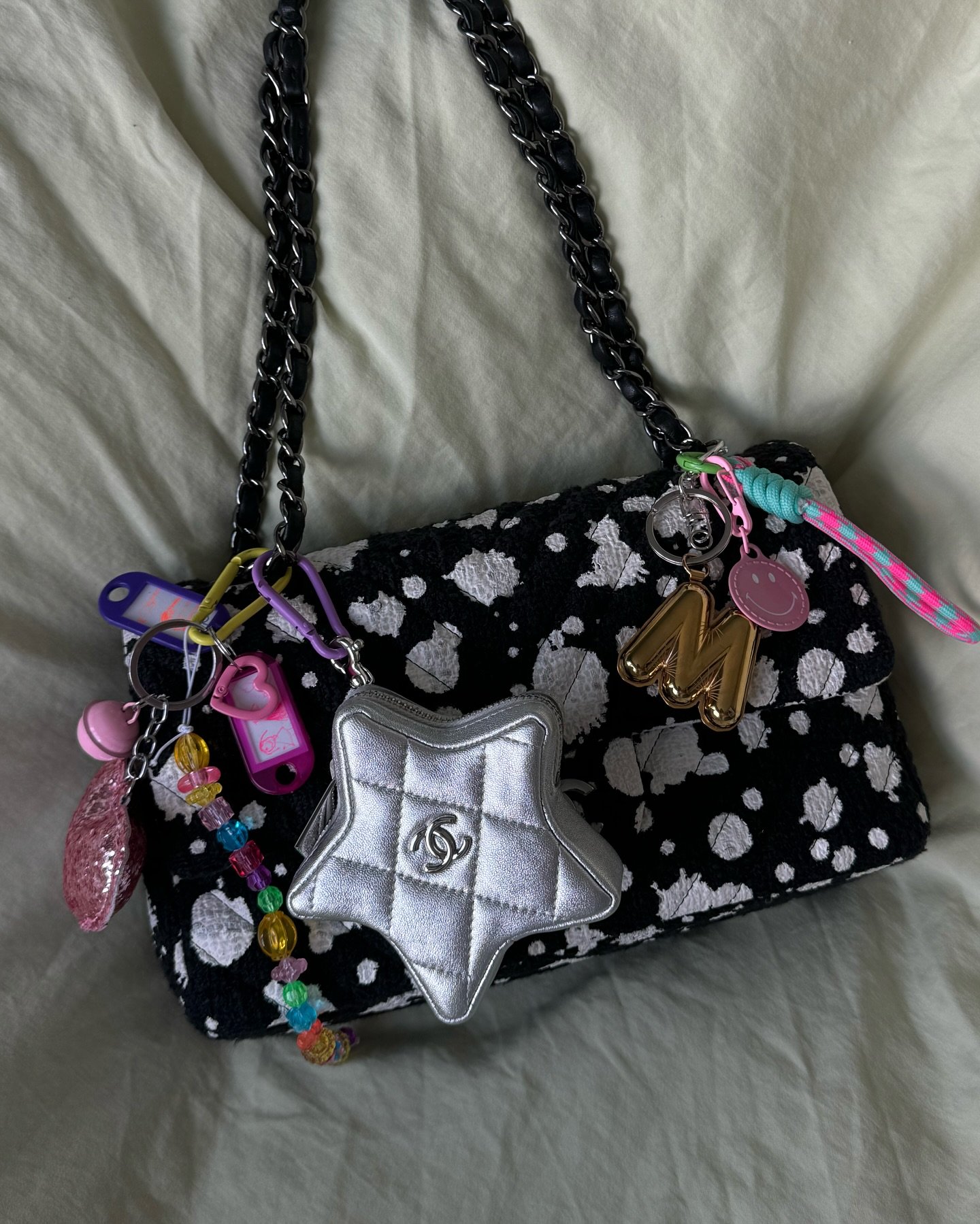 Bolsa preta com estampa de manchas brancas e alça de corrente preta. Decorada com acessórios coloridos, pingentes dourados, estrelas prateadas e chaveiros em estilo Kawaii. Tendência de moda eclética e divertida, misturando elementos clássicos com detalhes modernos.