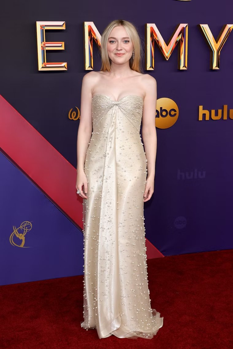 Pessoa vestida com um vestido longo de cor creme, tomara que caia, adornado com pequenos bordados e apliques brilhosos. O visual é elegante e sofisticado, ideal para eventos de gala ou premiações. Emmy 2024.