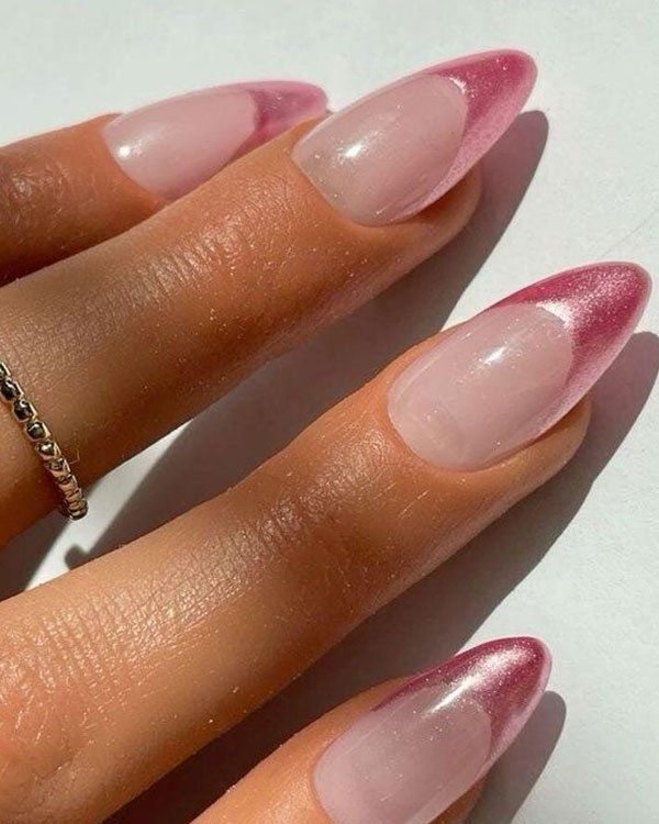 Unhas com formato amendoado e alongado, decoradas com esmalte em tonalidade pink metalizado na francesa. Tendência moderna em nail art, combinando elegância e ousadia. Anel minimalista complementa o visual.