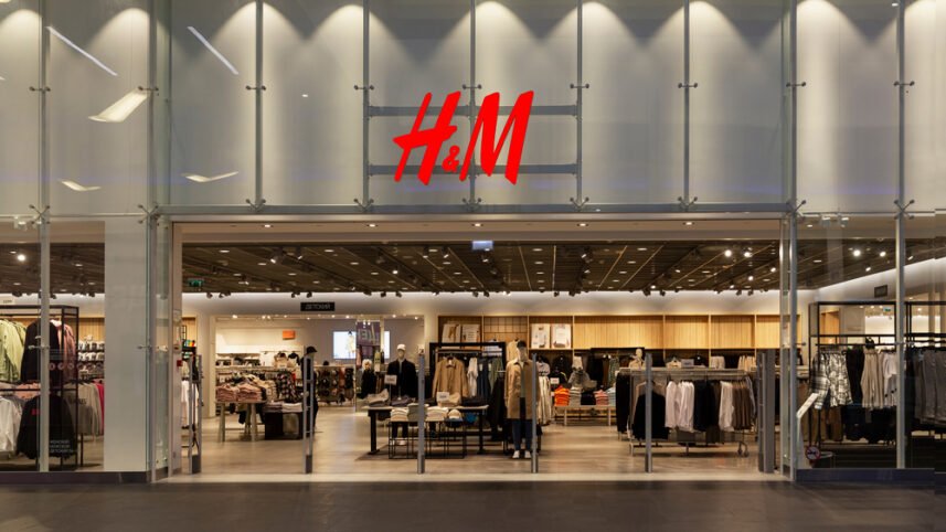 Loja H&M com manequins exibindo roupas da moda atual. Tendências incluem casacos, blazers, camisas, e roupas casuais. Cores neutras e peças básicas são predominantes, destacando um estilo casual e contemporâneo. Layout moderno e organizado.