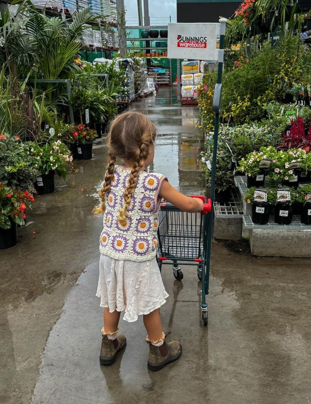 Criança usando colete de crochê florido, vestido branco fluido e botas infantis de couro. Estilo boho infantil em alta, combinando peças artesanais e rústicas. Influencer de moda infantil.