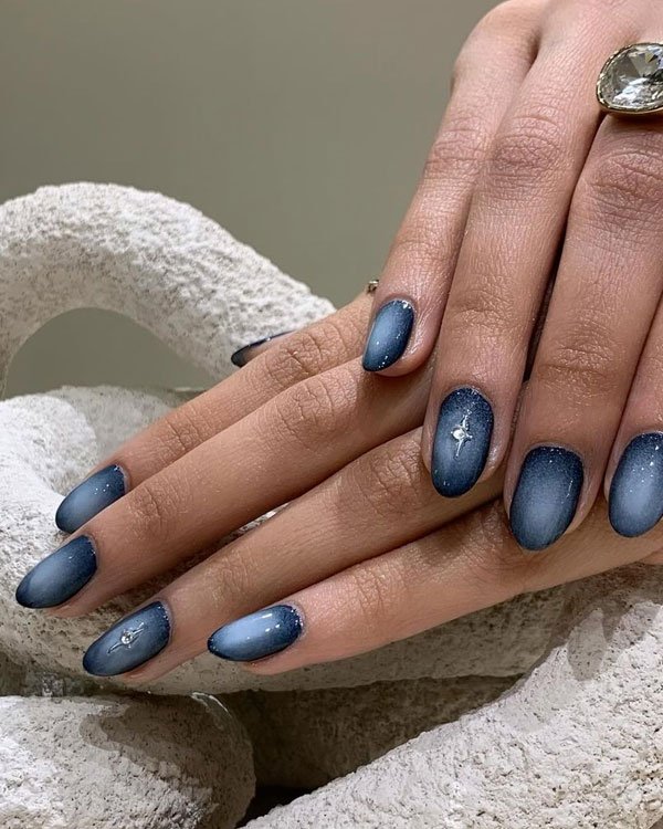 Unhas decoradas com esmalte degradê azul, tendência de moda em nail art. Destaque para detalhes de brilho e aplicação de pequenas pedras, unindo elegância e modernidade.