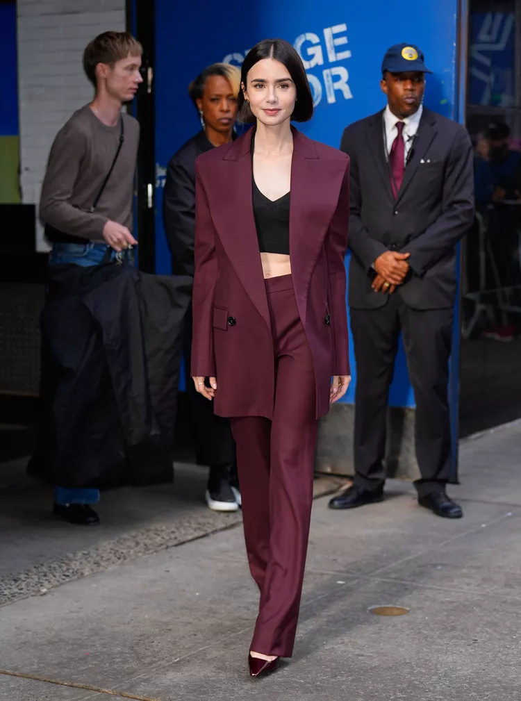 Mulher elegante vestindo terno vinho composto por blazer oversized e calça social reta, com top preto por baixo. Look sofisticado e moderno, exemplificando a tendência do power suit feminino em tons ousados.