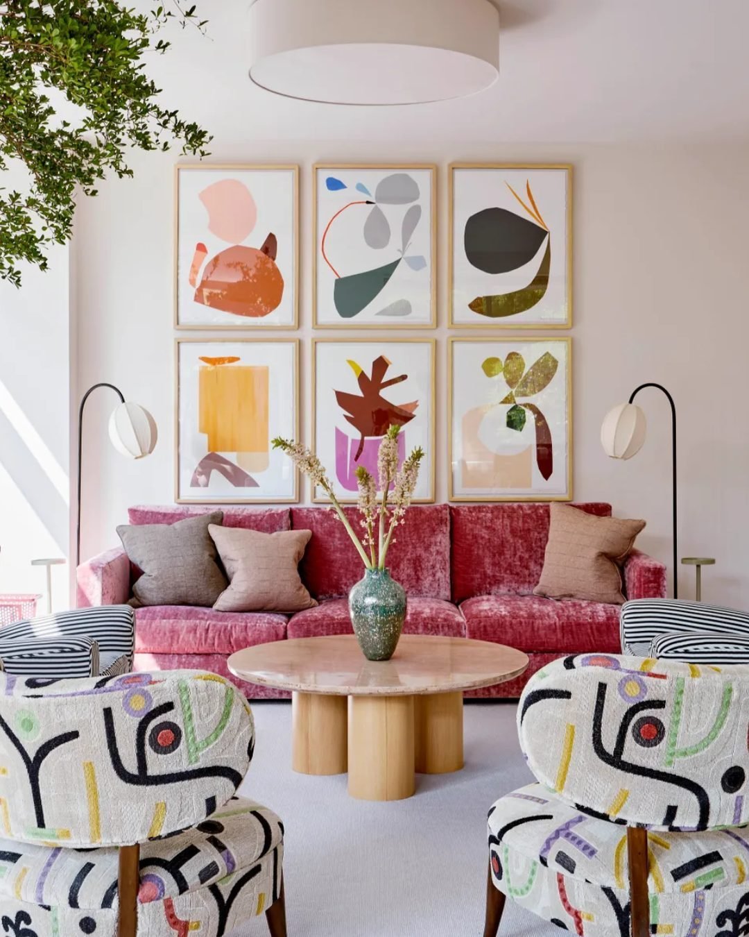 Sala de estar moderna com sofá de veludo rosa, poltronas com padrões geométricos contemporâneos e mesa de centro de madeira. Parede com quadros abstratos vibrantes. Decoração integra tendências de design escandinavo e mid-century, luminária de piso