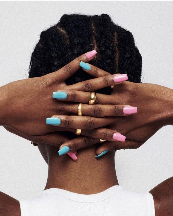 Imagem destacando mãos femininas com unhas longas e coloridas em tons pastéis de rosa e azul. A pessoa também usa anéis dourados, complementando um estilo moderno e elegante.