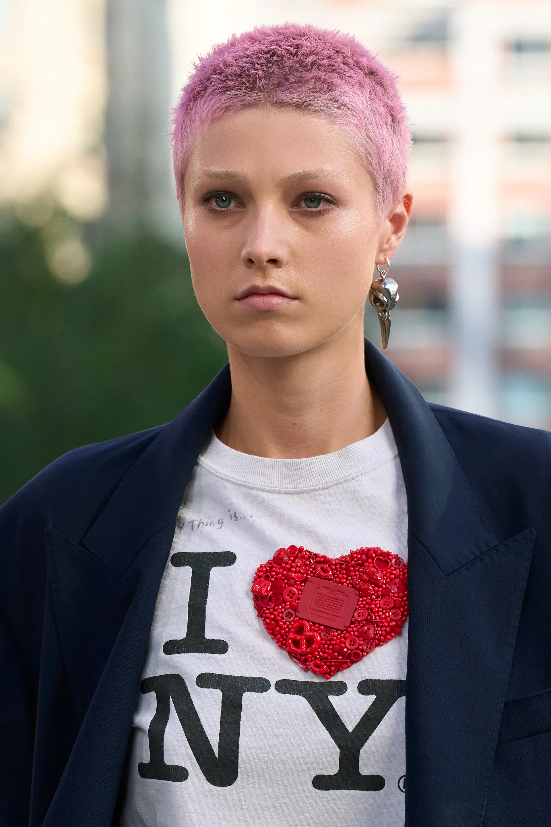 Pessoa com cabelo curto rosa, usando camiseta branca 