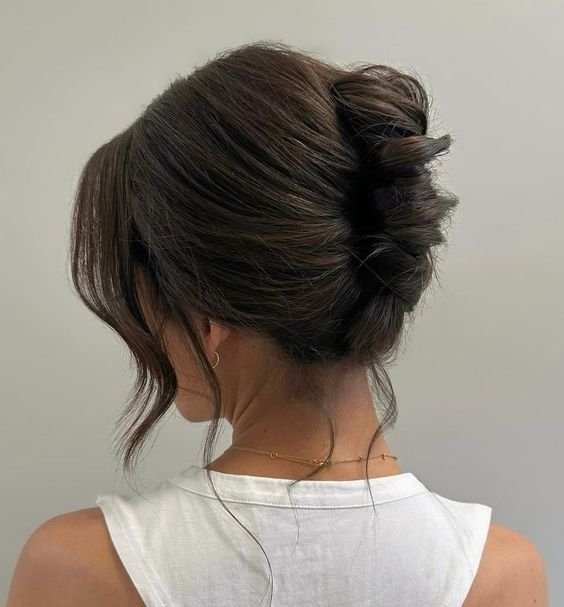 Imagem de uma mulher de costas usando uma blusa branca sem mangas. penteado do momento cabelo preso em um coque despojado e elegante, com algumas mechas soltas. O visual é complementado por um brinco discreto e um colar delicado, representando um estilo casual chic.