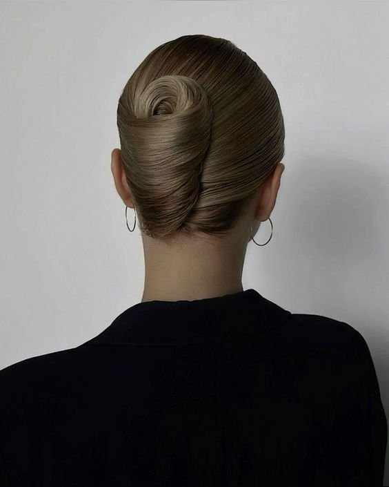 Penteado elegante com coque enrolado, cabelo loiro, liso e bem preso. Vestimenta preta, sofisticada, e brincos de argola prata completam o visual minimalista e refinado. Tendências de moda focando em simplicidade chic e acessórios clássicos. penteado do momento