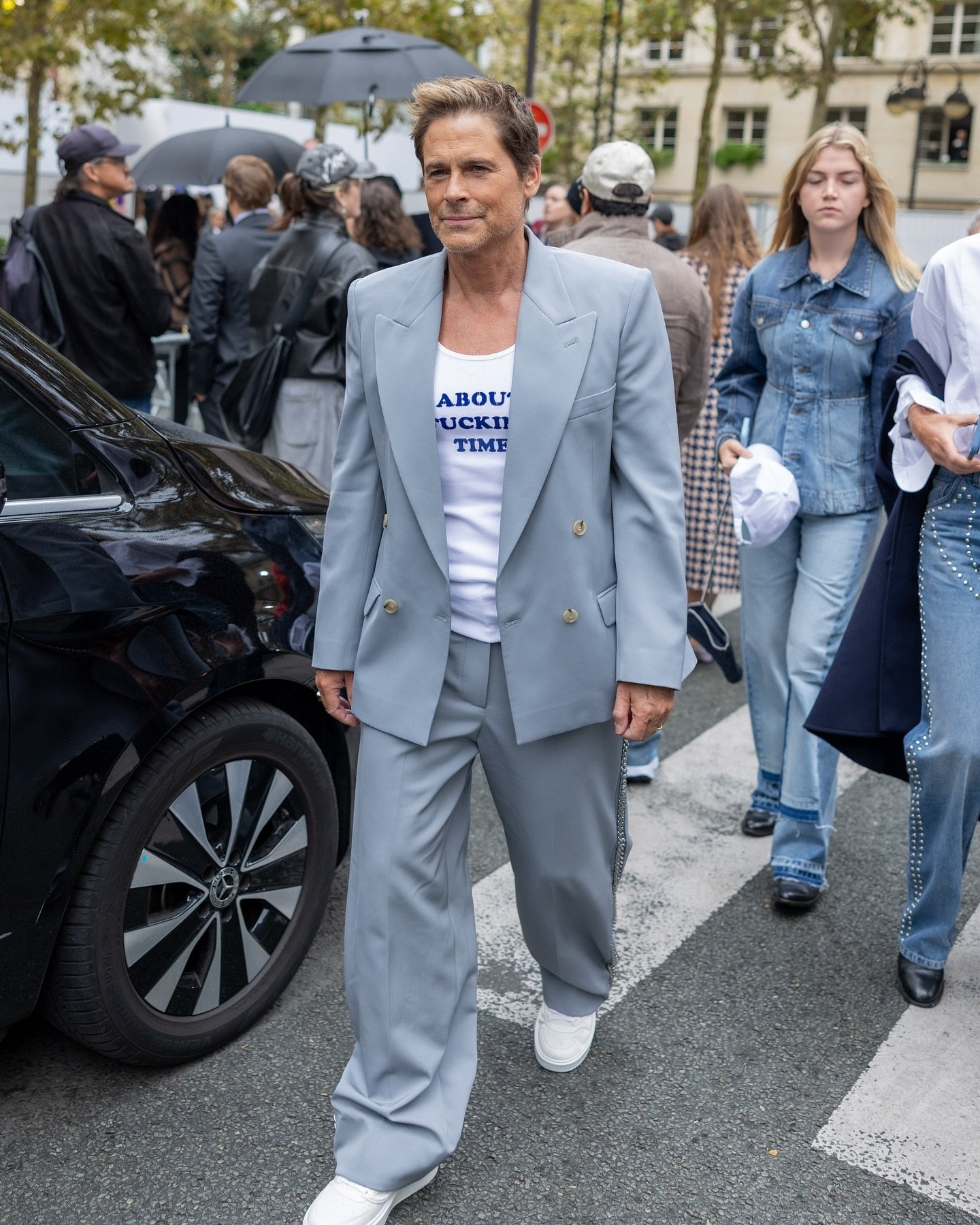 Homem vestindo terno cinza oversized, camiseta branca com estampa e tênis branco. Moda urbana elegante, combinando conforto e estilo casual. tendência de terno largo, alfaiataria desconstruída e combinação de peças formais com elementos esportivos.