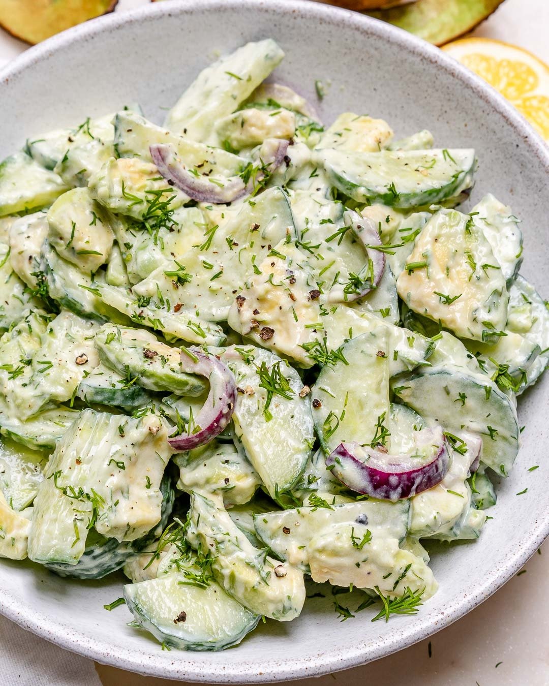 Salada de pepino com cebola roxa e iogurte. Prato é decorado com ervas frescas e pimenta moída. Ideal para dias quentes e refeições leves. Receita saudável e nutritiva, rica em fibras e sabor.