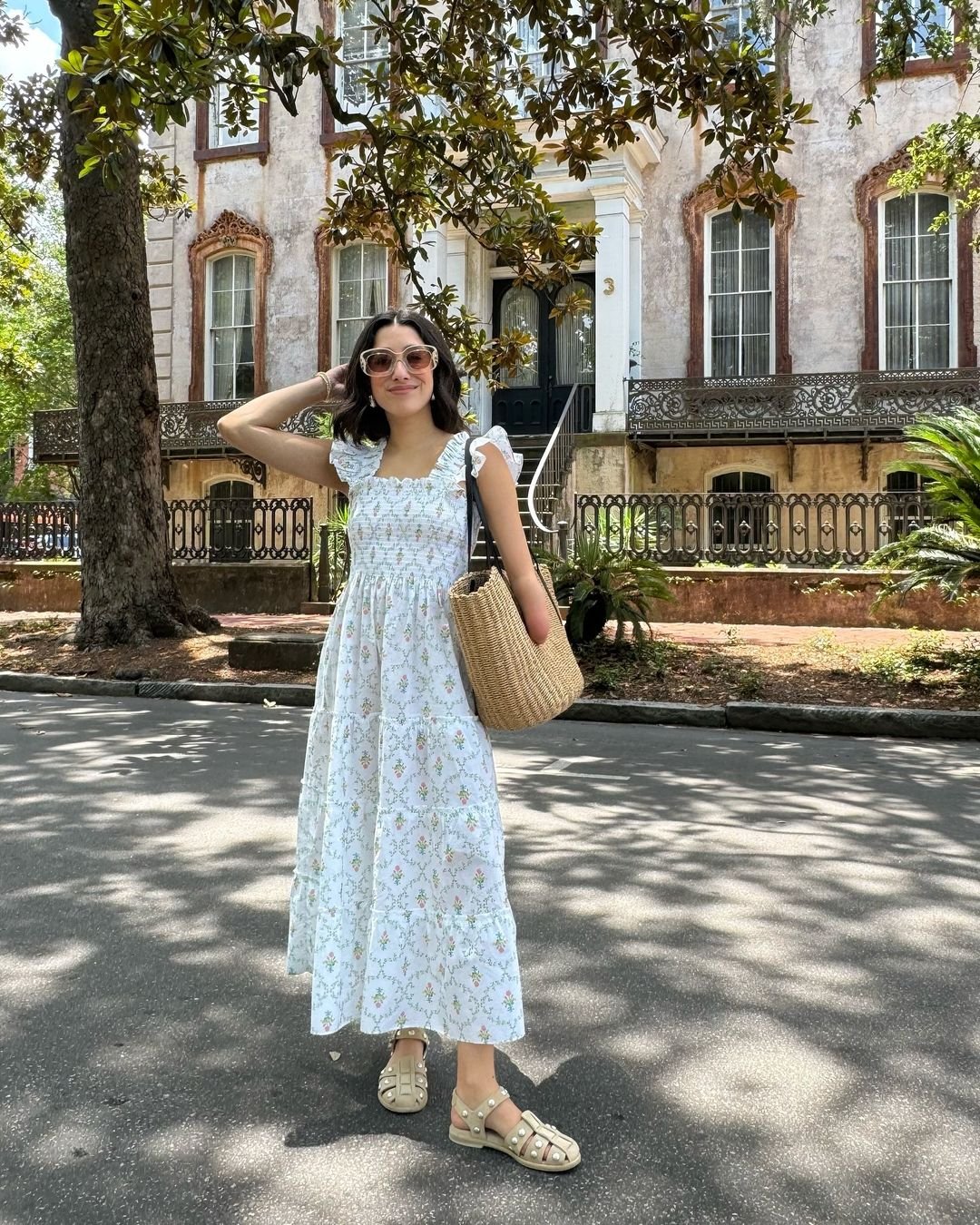 Mulher usando vestido longo floral de verão, estilo romântico, óculos de sol e sandálias claras. Bolsa de palha complementa o look descontraído e natural. Ideal para passeios ao ar livre e dias de calor.