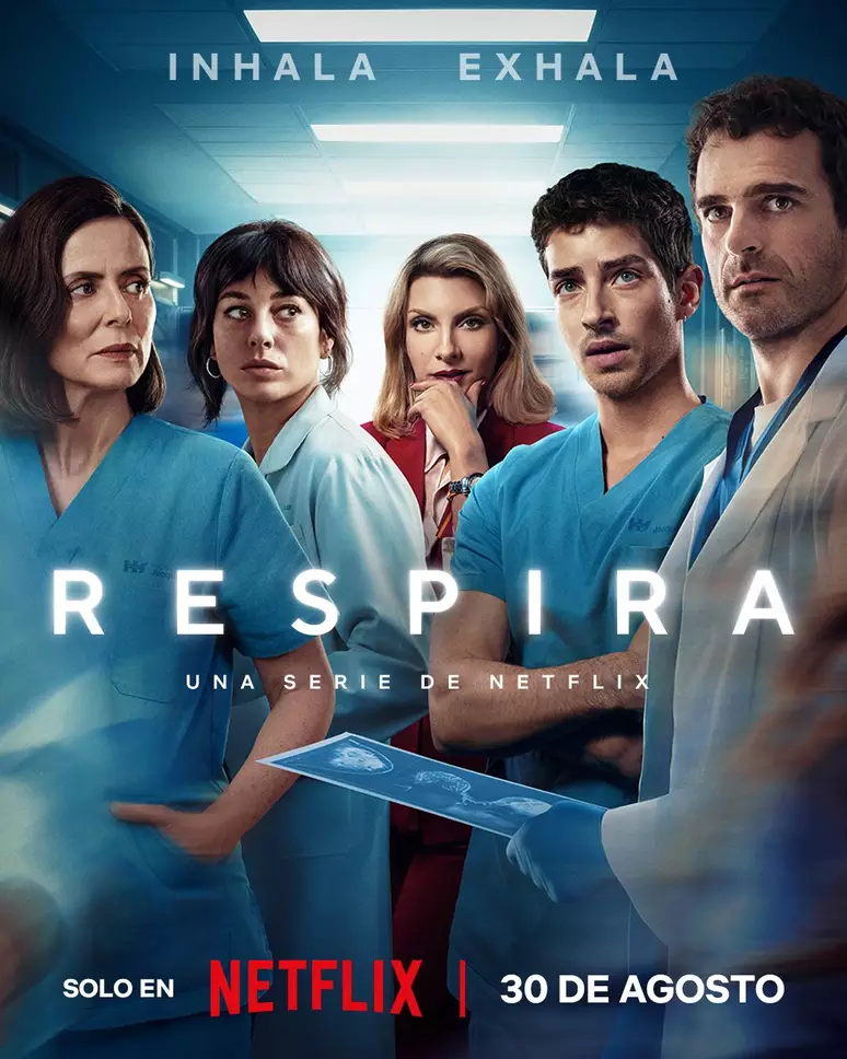 Imagem de série médica onde personagens vestem jalecos e uniformes hospitalares azuis. Um deles destaca-se com blazer vermelho, representando autoridade ou cargo superior. Séries novas para maratonar.