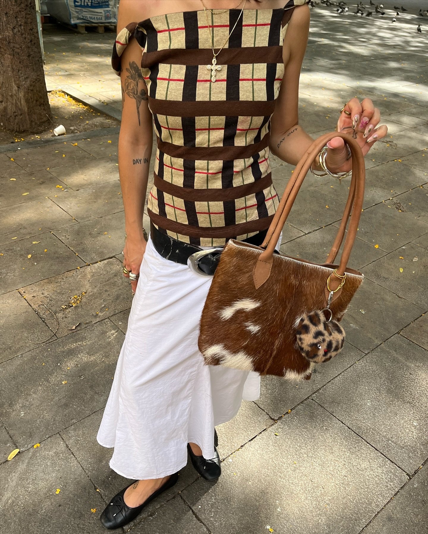 Bolsa com estampa cow print combinada a uma saia branca e blusa xadrez em estilo casual.