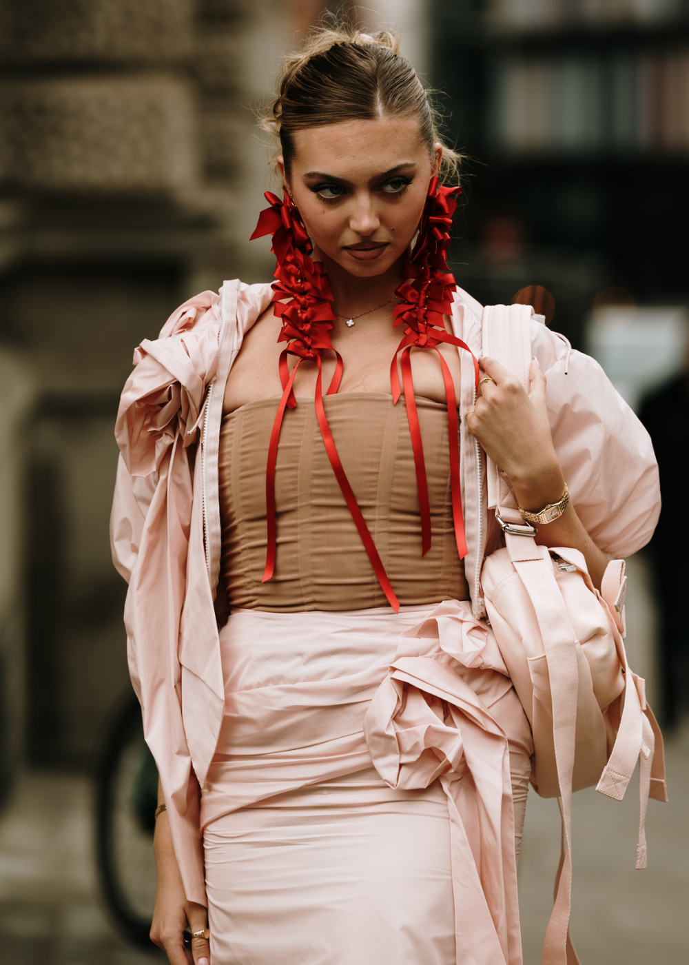 Moda urbana: Look sofisticado com vestido nude, trench coat rosa claro e brincos extravagantes vermelhos com fitas. Combinação de tons neutros com acessórios marcantes, tendência atual em alta costura e street style contemporâneo.