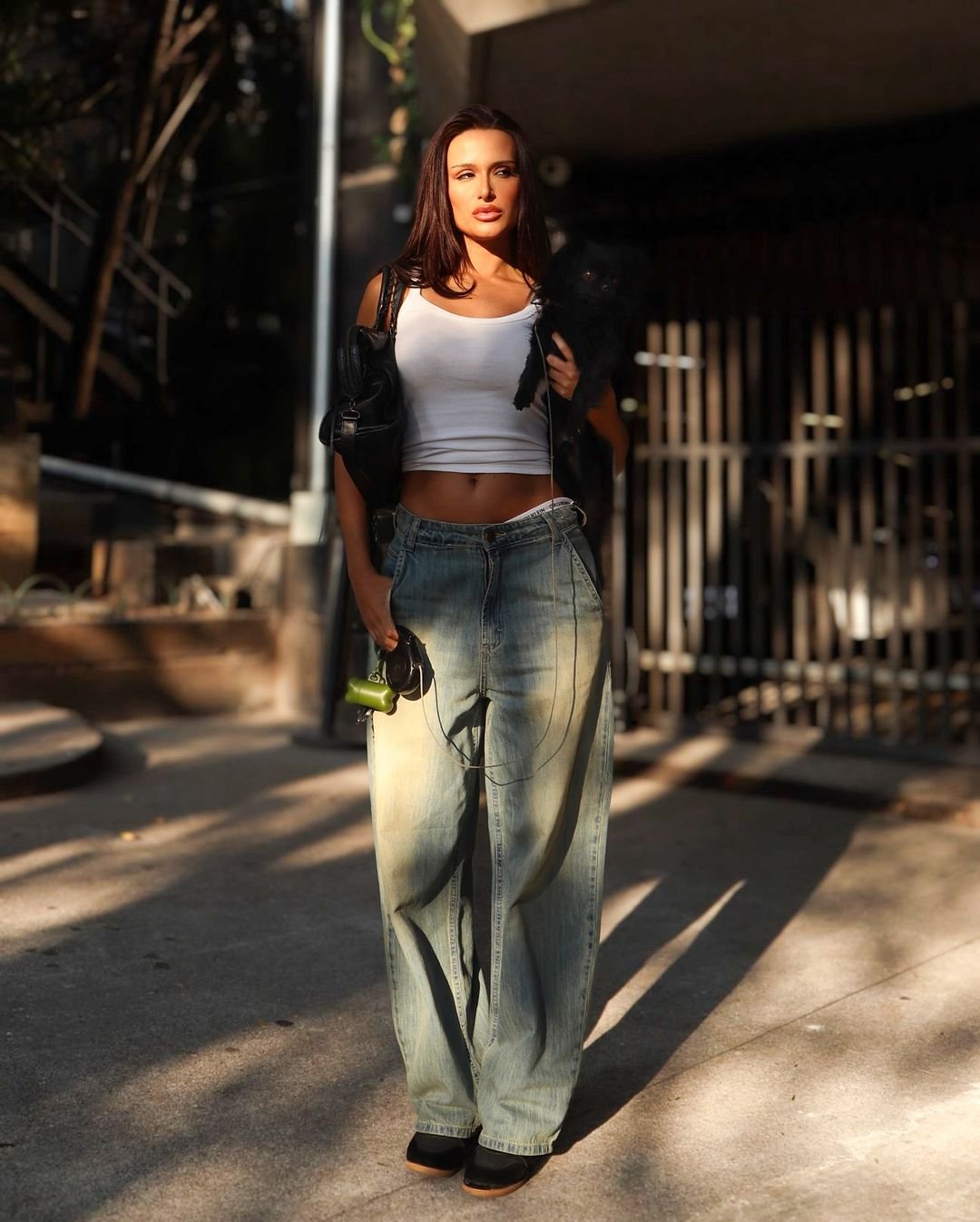 Mulher vestindo tendência casual com calça jeans de modelagem larga e desbotada e cropped branco. Completa o look com jaqueta preta e sapatos pretos. A moda aposta no estilo confortável e despojado, ideal para o dia a dia. tênis de salto