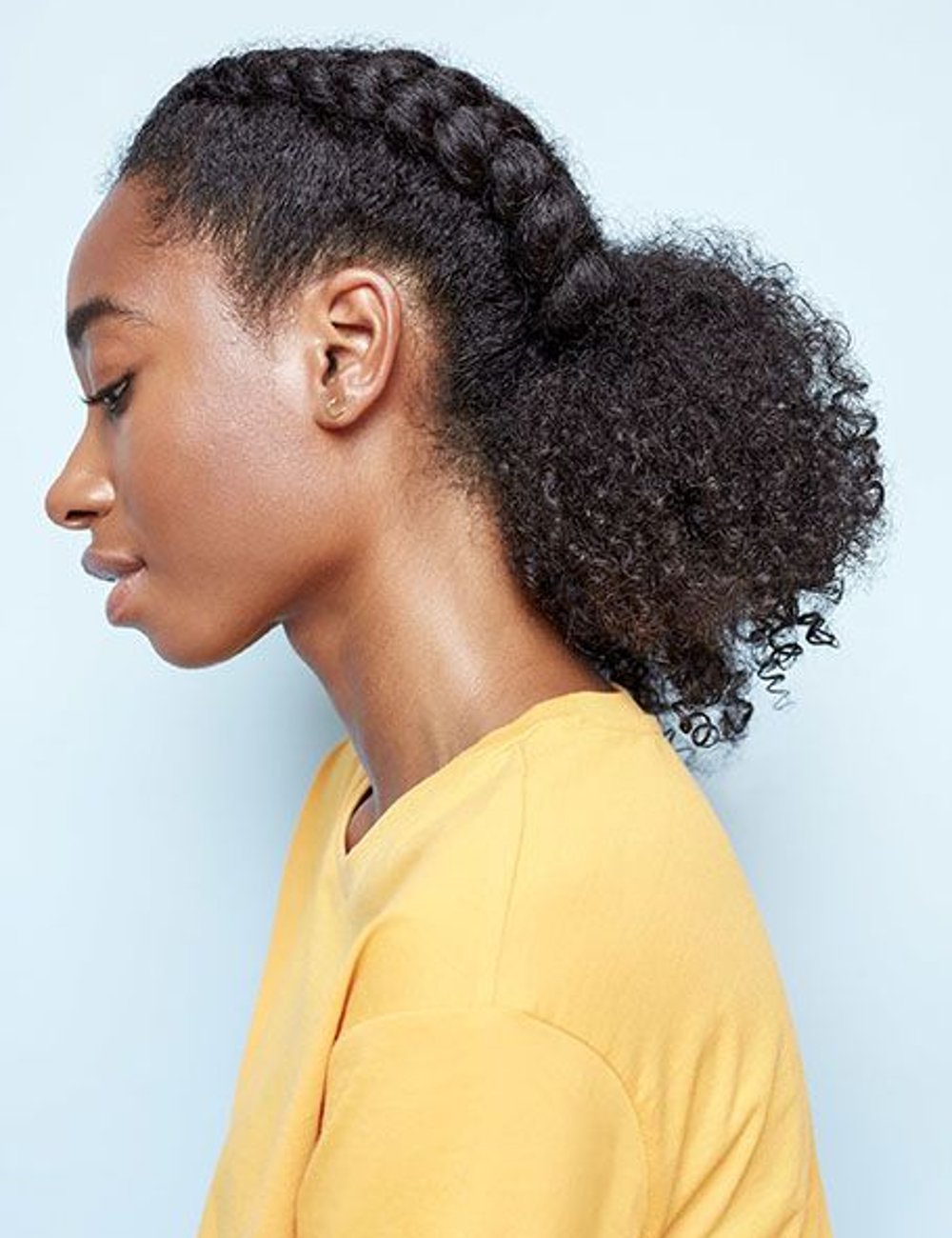 Jovem com camiseta amarela e cabelo com trança boxeadora. Look casual e moderno, destacando penteados protetores e moda minimalista. Perfeito para realçar estilo autêntico e conforto no dia a dia.