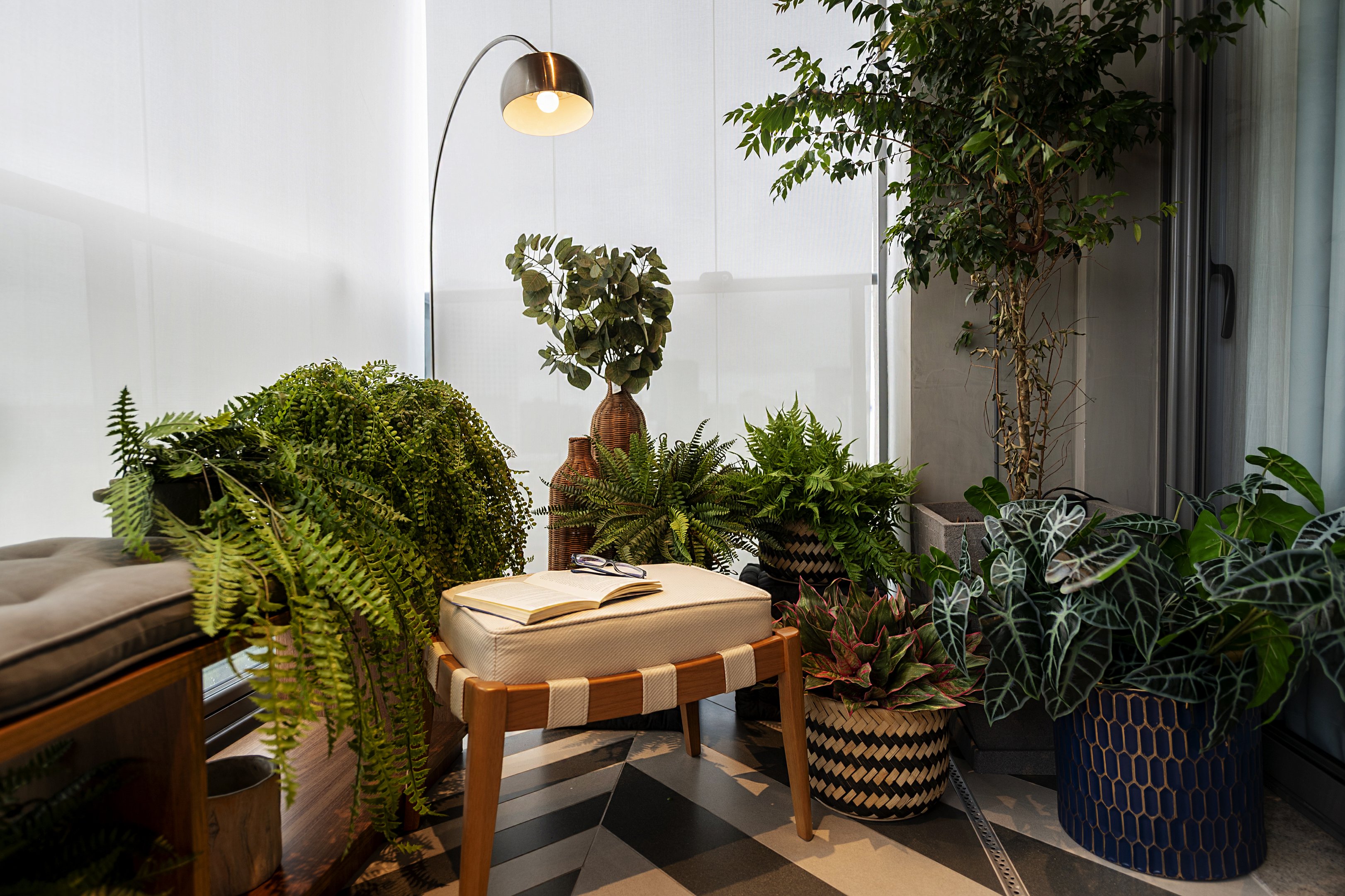 Sala de apartamento decorada com várias plantas ao lado de uma janela e uma luminária.