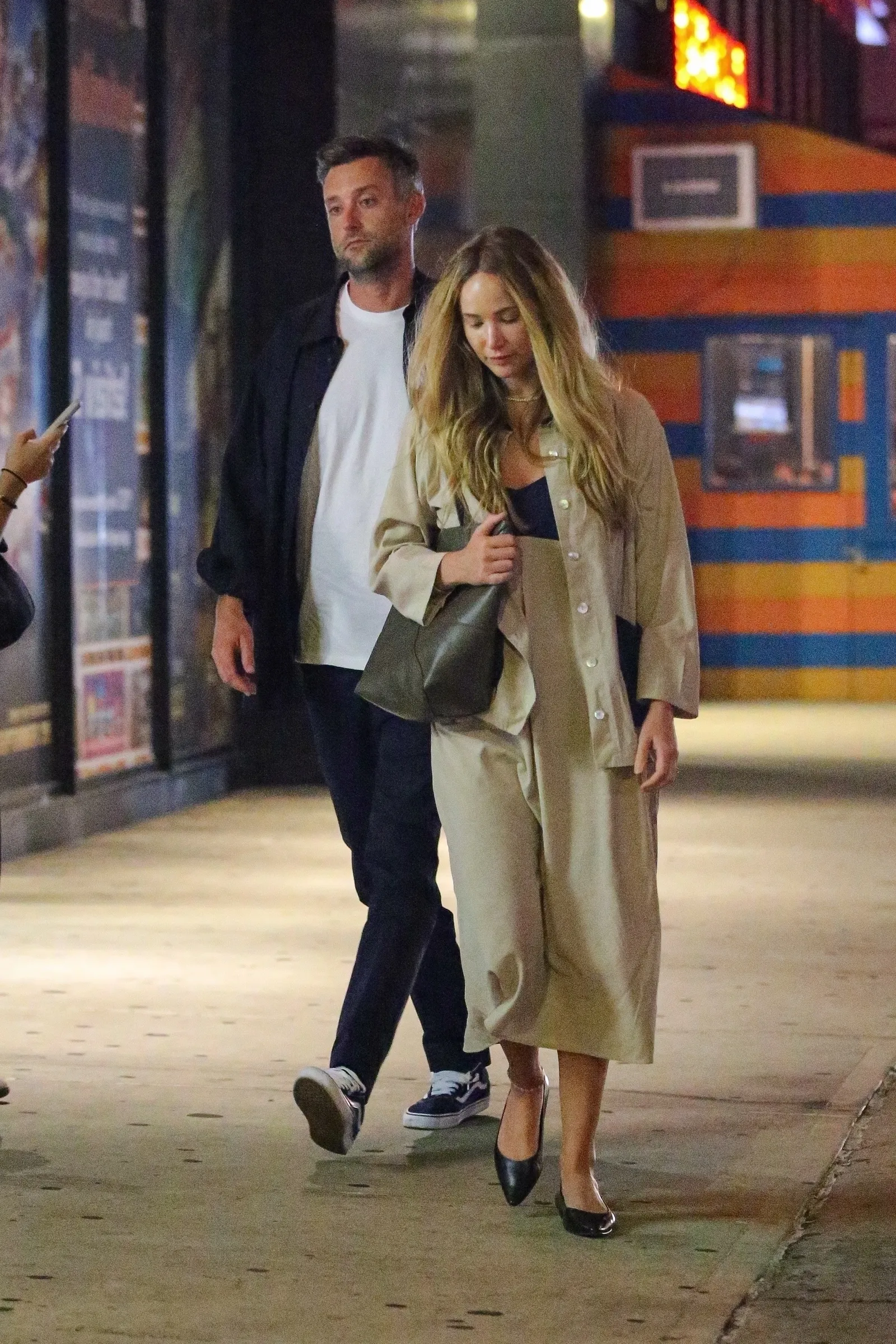 Casal caminhando à noite, mulher grávida com conjunto bege elegante, exemplo de look básico de grávida.