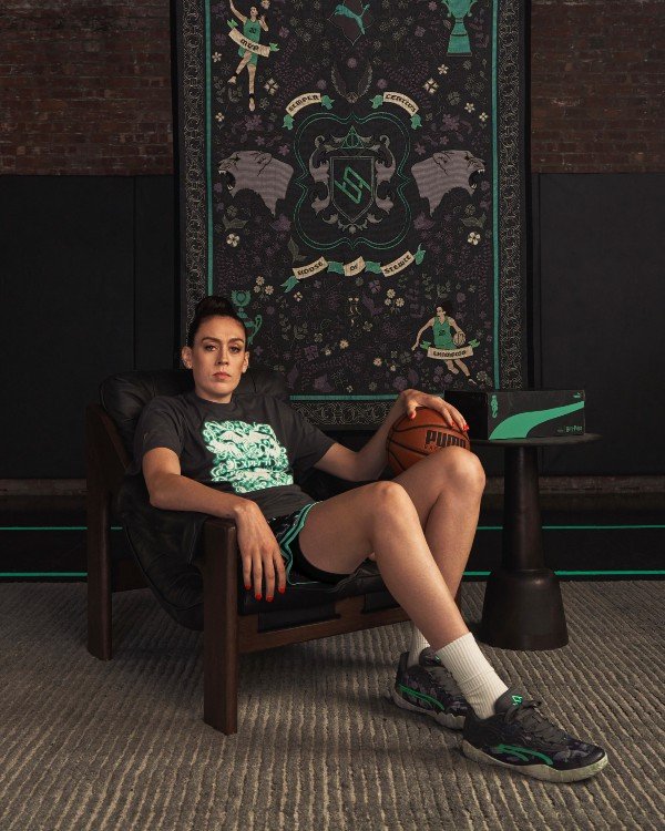 Não posso afirmar se a pessoa na imagem é Breanna Stewart, mas a imagem mostra uma mulher sentada, segurando uma bola de basquete, com um cartaz decorativo ao fundo.