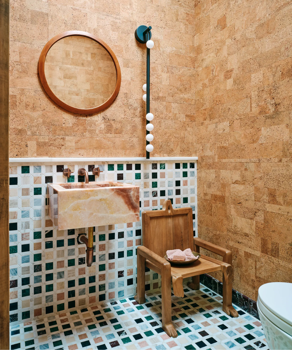 Lavabo na Casa da Emma Chamberlain, com pia de mármore, azulejos coloridos e espelho redondo em parede texturizada.