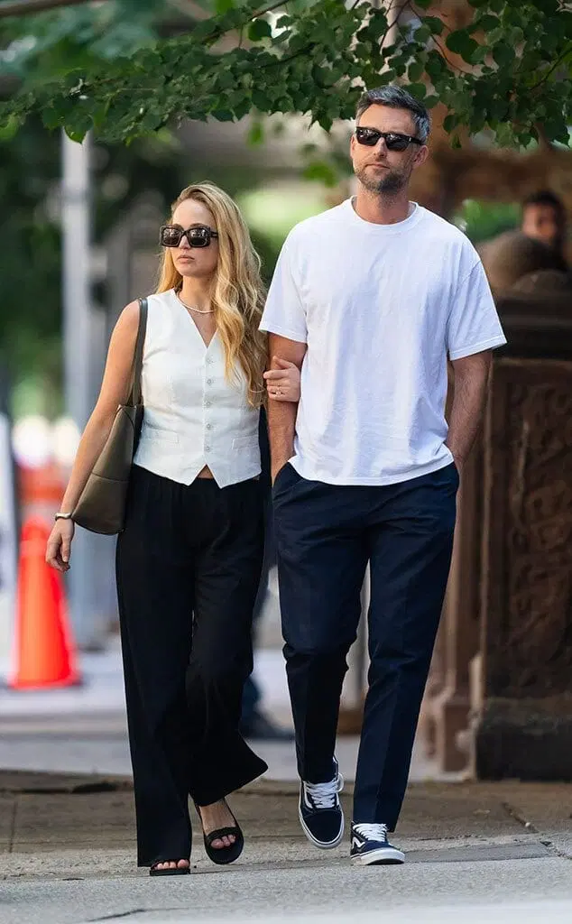 Homem e mulher caminhando de mãos dadas, vestindo roupas casuais e óculos escuros. Ambos aparentam conforto e estilo urbano.