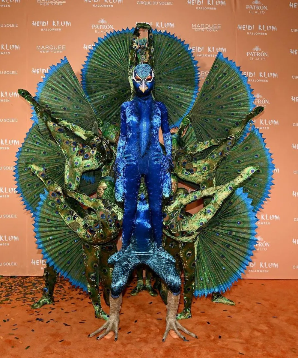 Figurino deslumbrante de pavão, com traje azul cintilante e detalhes realistas em verde e penas exuberantes. Este look inusitado mistura fantasia e extravagância, ideal para eventos temáticos. Destaque para a criatividade e detalhes detalhados.