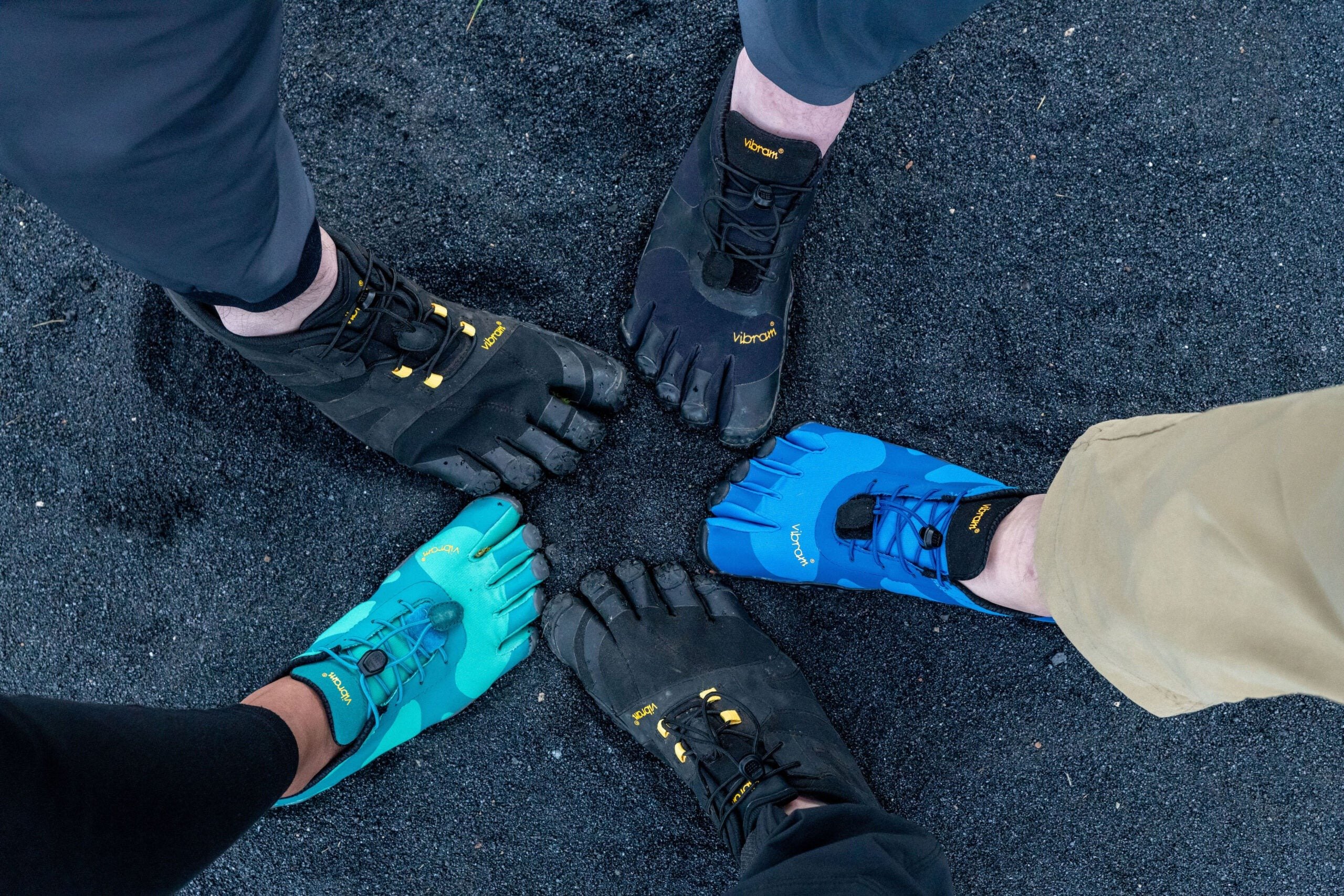 Pés enfileirados em calçados minimalistas Vibram de diferentes cores, tendência que foca no naturalismo e conforto. Perfeitos para atividades ao ar livre, combinam estilo esportivo com inovação em design ergonômico.