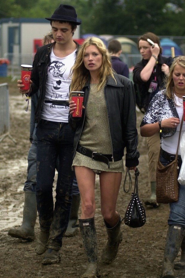 Festival fashion: estilo casual e despojado. Vestido curto com jaqueta preta e cinto largo. Botas de borracha, tendência prática para eventos ao ar livre. Acessório de bolsa pequena completa o look festivo e moderno.