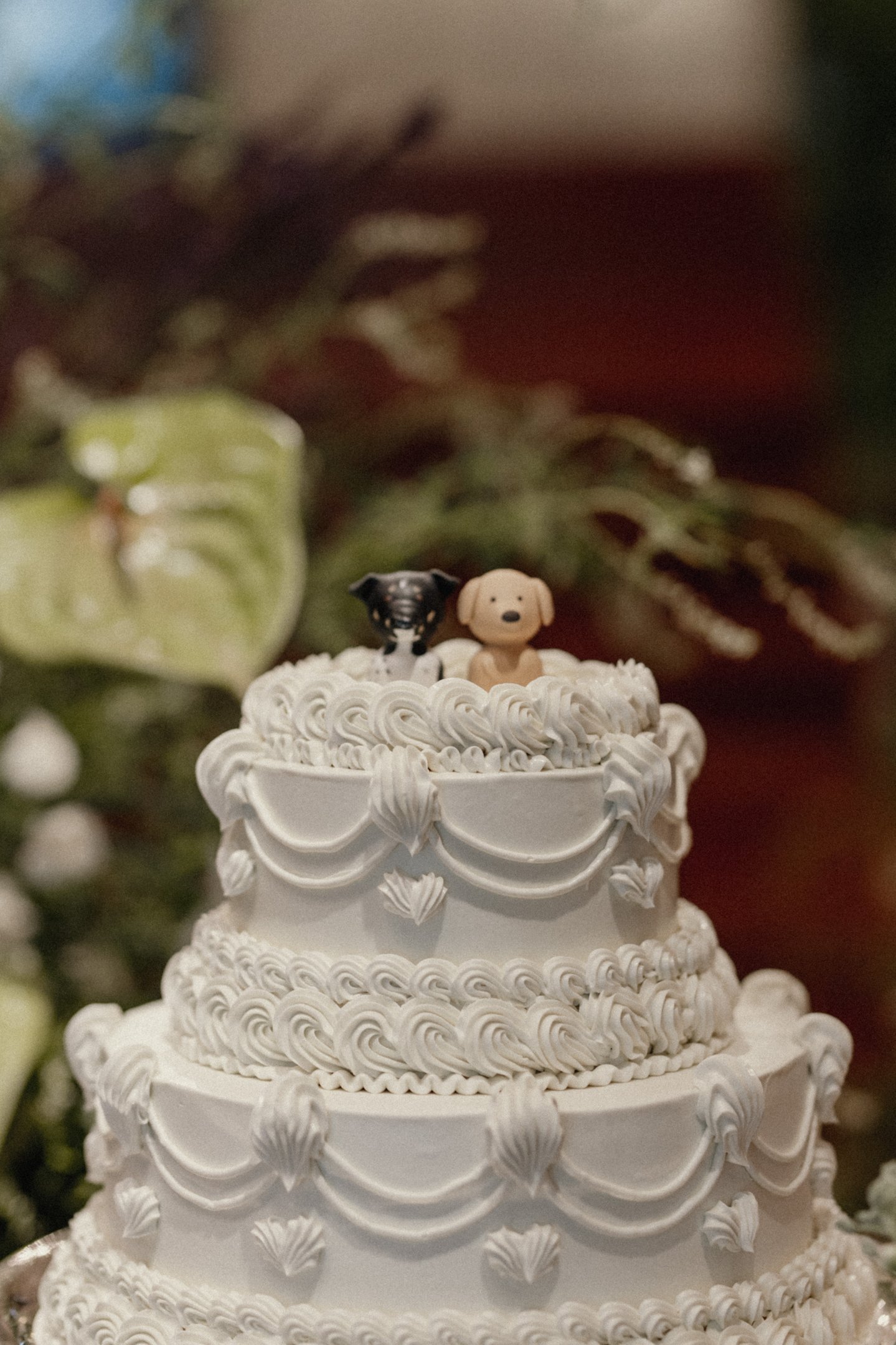 Topo de bolo de casamento com miniaturas de cães, destacando uma tendência moderna e divertida em decorações de eventos. O bolo exibe detalhes clássicos em creme, mesclando elegância atemporal com elementos personalizados.