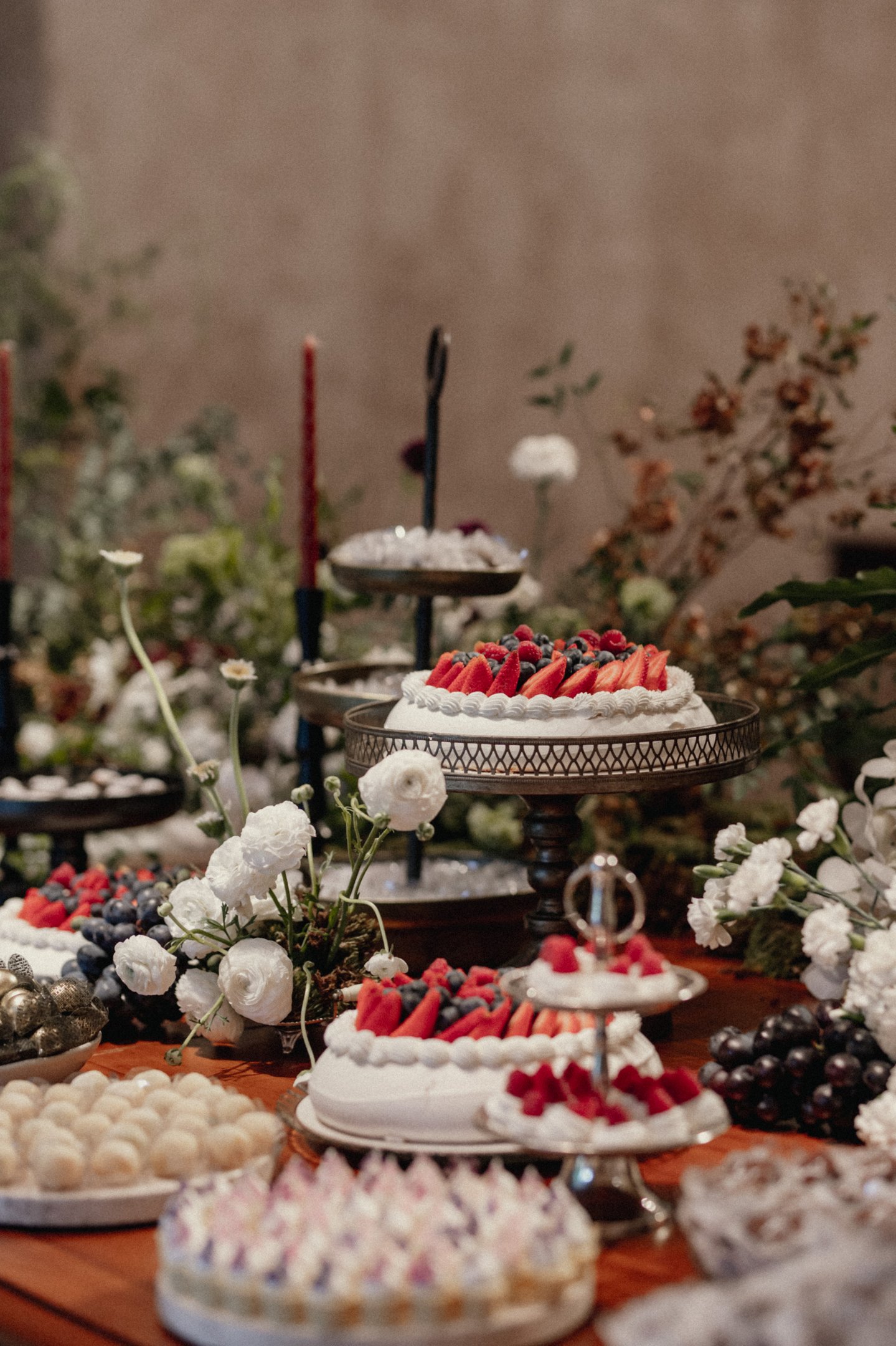 Imagem de uma mesa elegantemente decorada para festa com tendência vintage e rústica. Apresenta bolos com frutas vermelhas e arranjos de flores brancas, demonstrando um estilo sofisticado e natural.