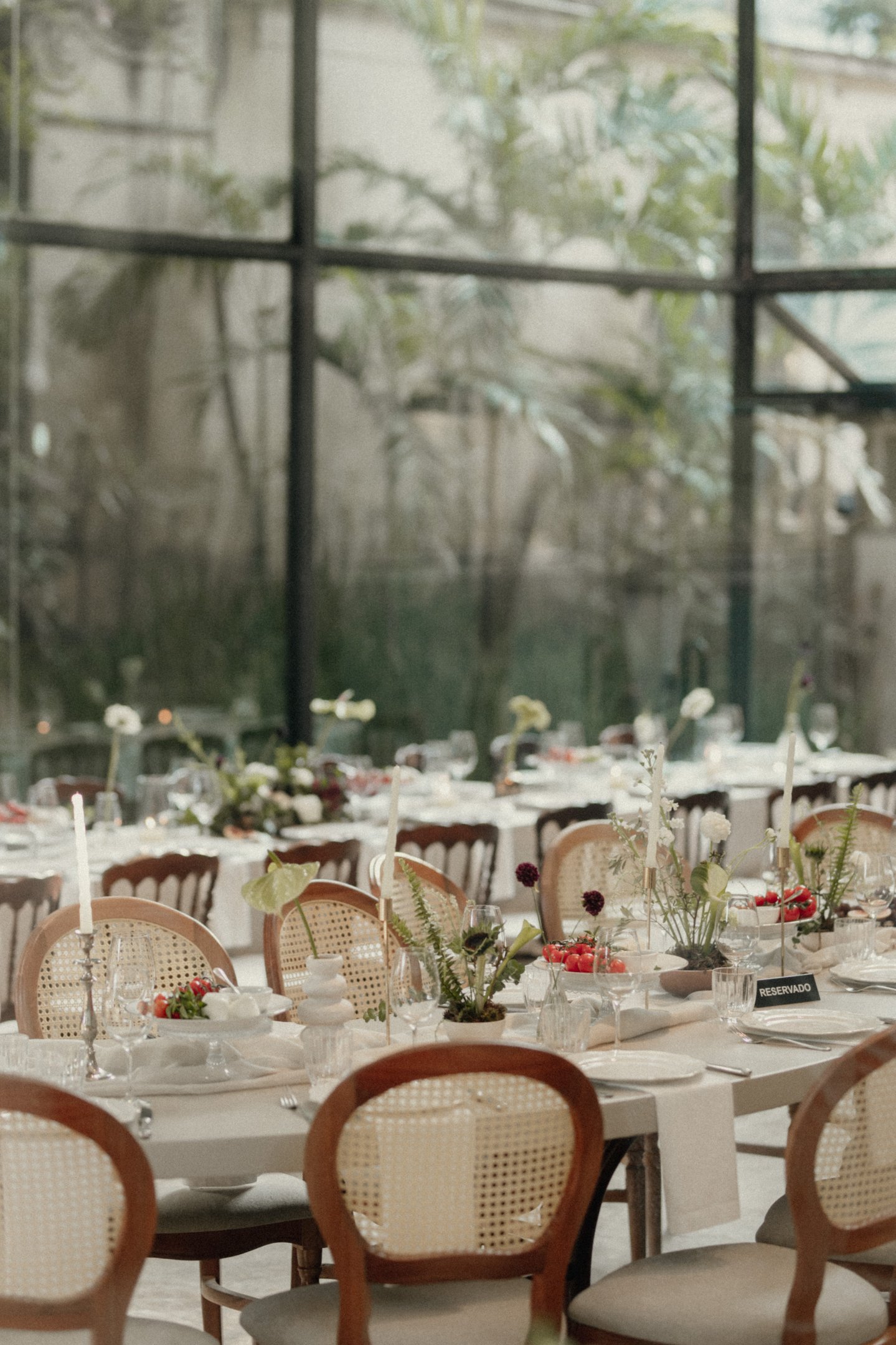 Mesa de jantar de casamento da Lela Brandão, com cadeiras de palha, arranjos florais minimalistas e velas. Estilo clássico e atemporal, ideal para eventos formais e casamentos. Decoração detalhada e harmoniosa.