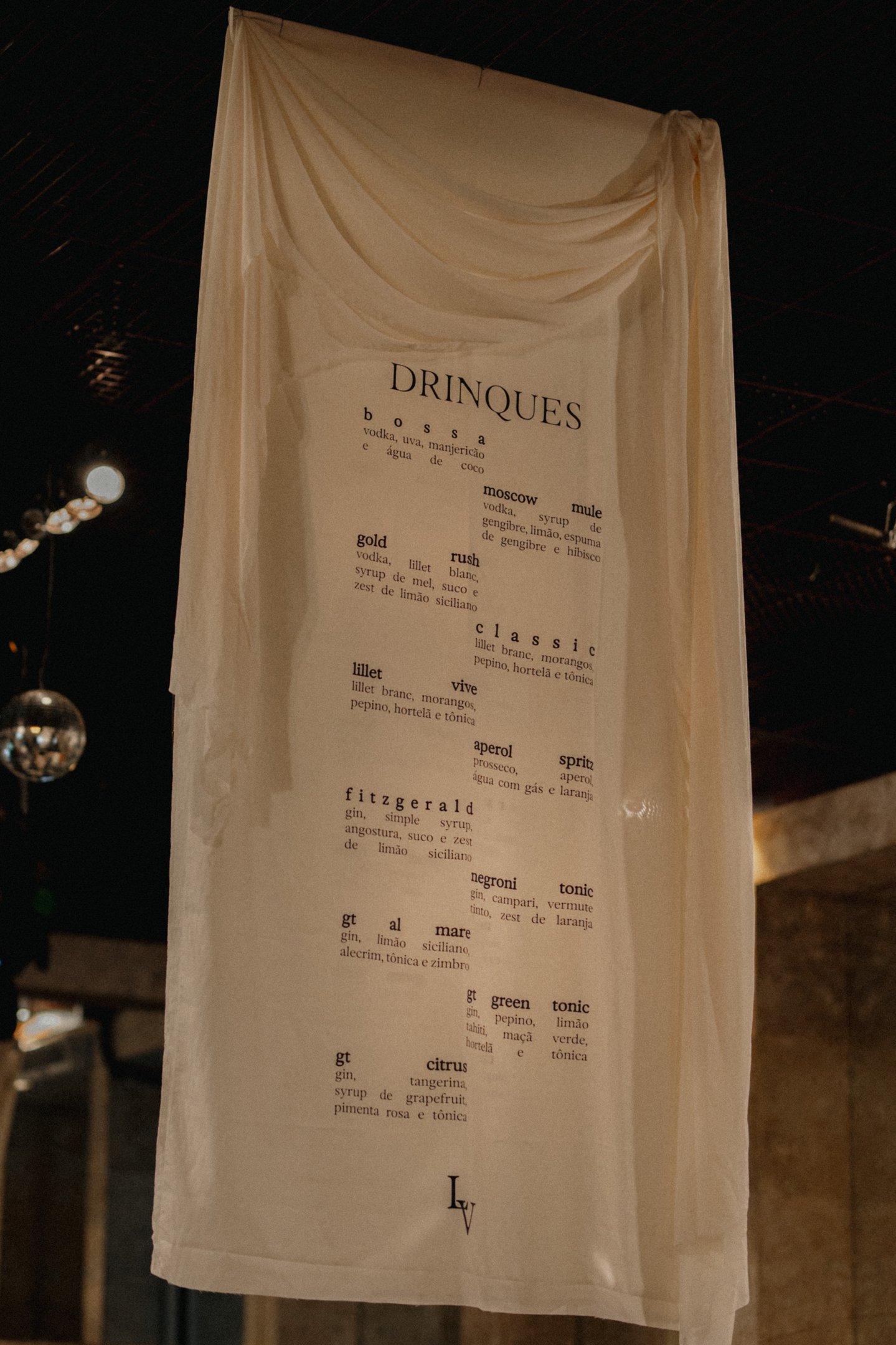 Imagem de um menu de drinques em tecido suspenso, com design minimalista e sofisticado, destacando-se em um ambiente intimista. Tendência de decoração moderna e clean, com foco em tipografia elegante e composição visual atrativa.