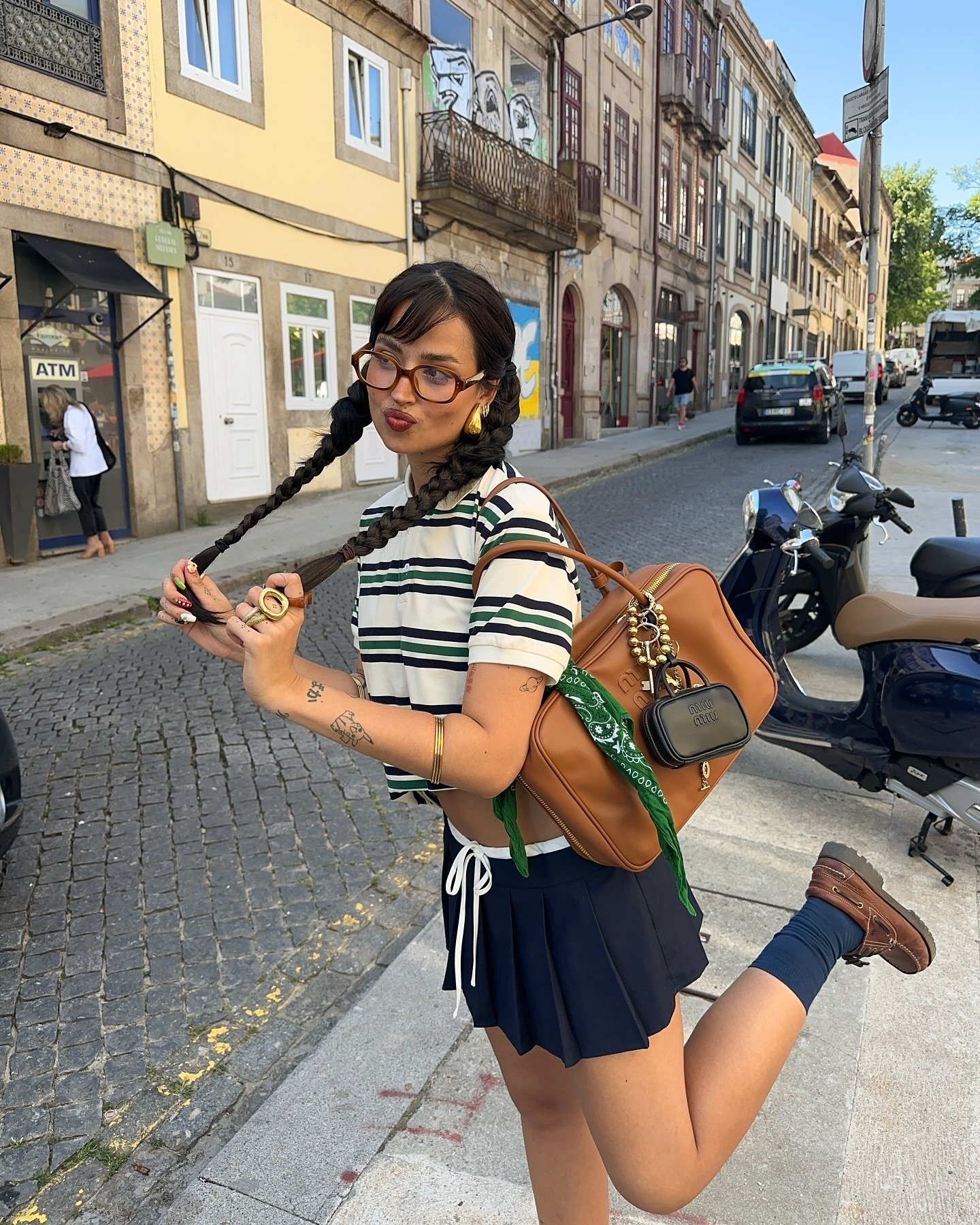 Pessoa sorrindo em rua, usando camisa polo listrada, saia preta e bolsa marrom no ombro.